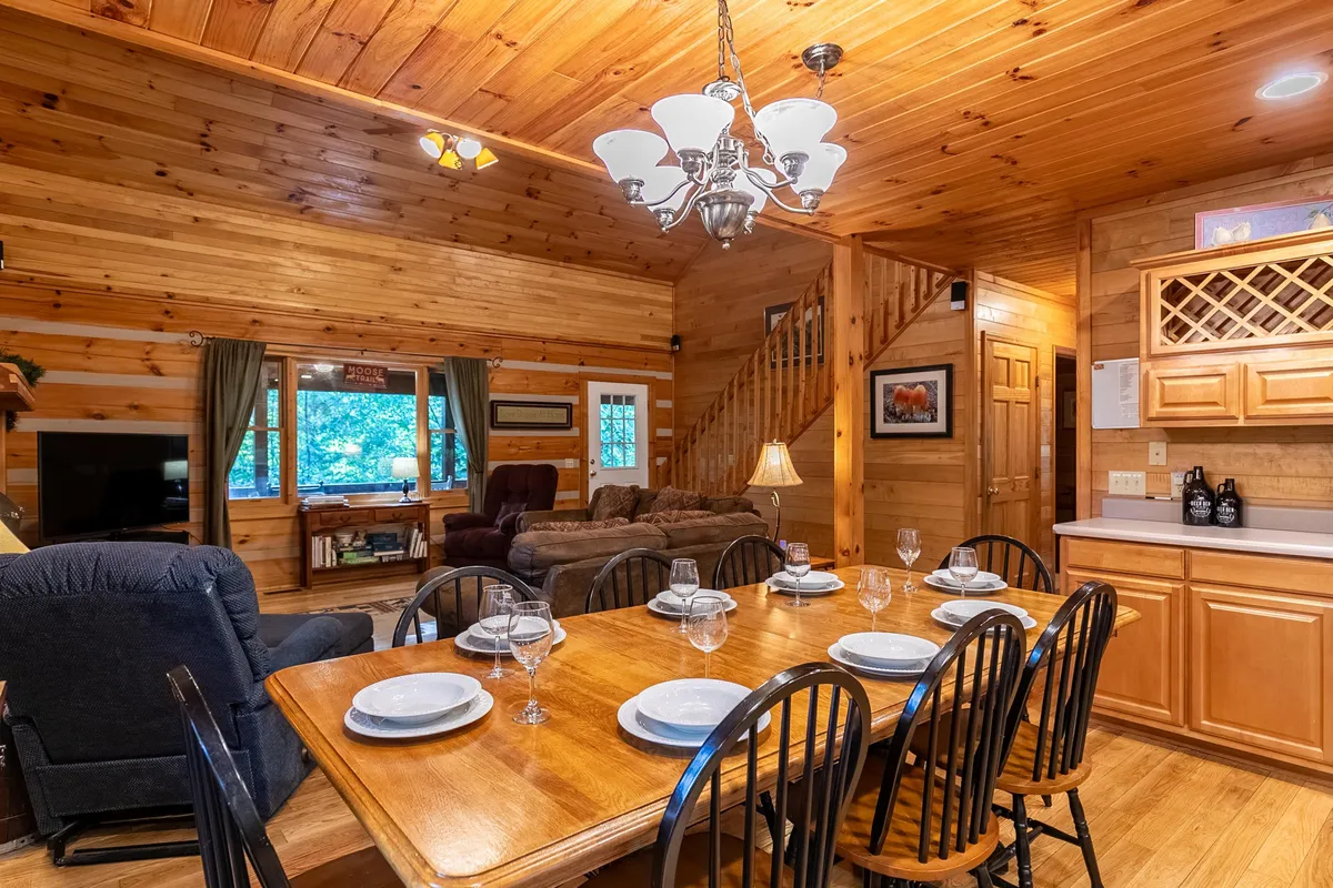 A dining and seating area filled with natural light, featuring a welcoming dining table, cozy sofa, and a large window to bring the outdoors in. The setup encourages communal gatherings and relaxing moments with pets and family alike.