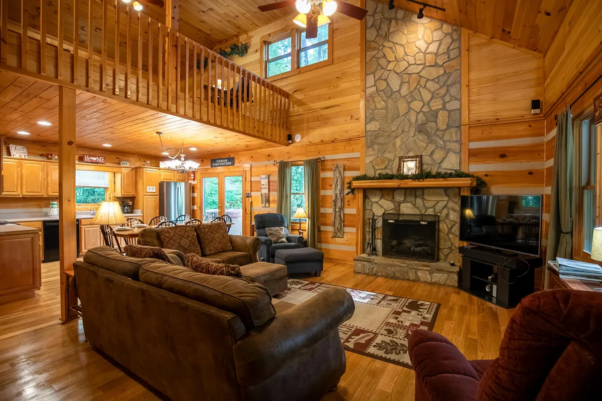 A spacious living area with a striking stone fireplace, exposed wooden beams, comfortable seating, and large windows that offer views to the outside. The arrangement is warm and inviting, ideal for unwinding after a day of outdoor exploration.