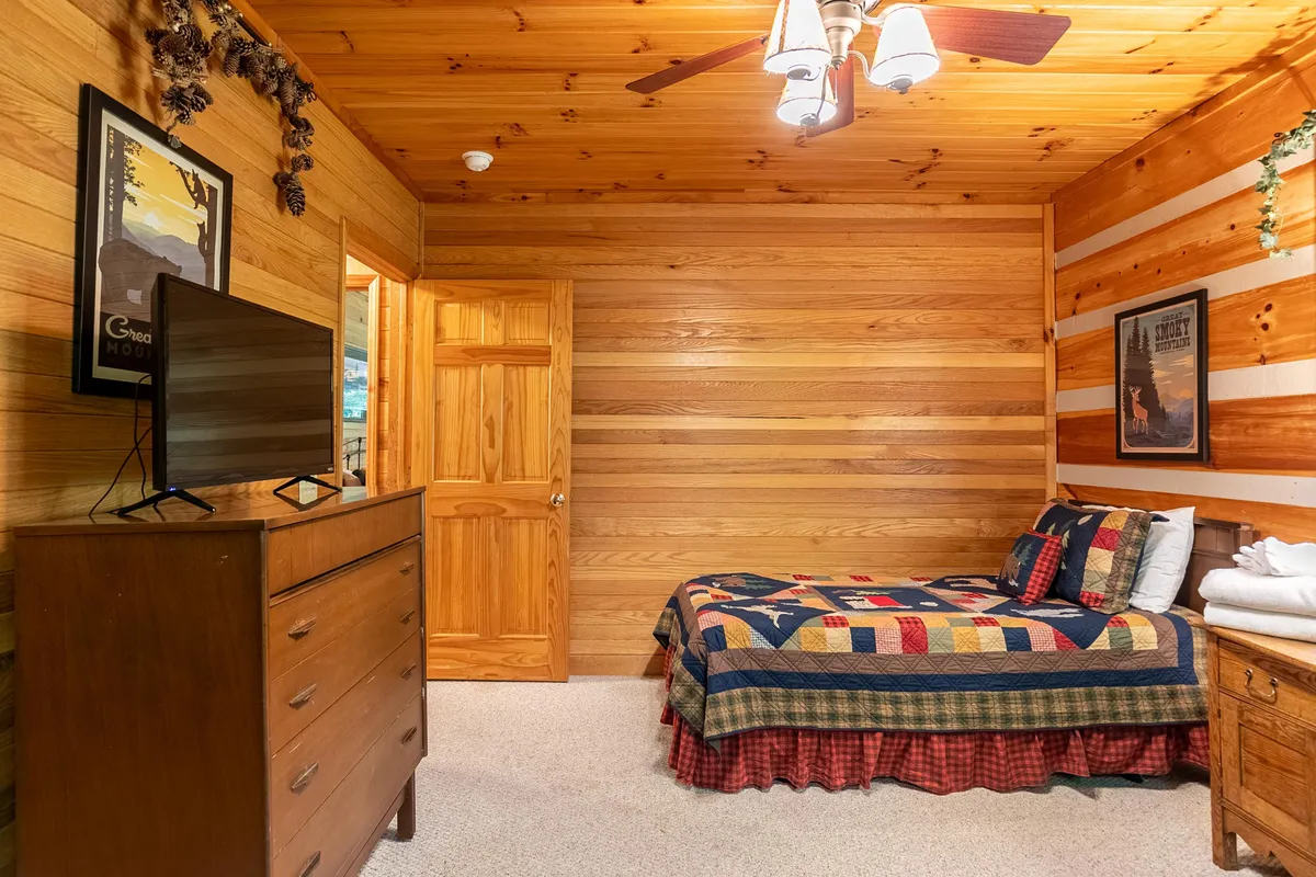 A warmly lit bedroom with a quilted bed, a wooden dresser, and a television positioned for relaxing movie nights. The decor is comfortable and inviting, suggesting a private retreat ideal for unwinding after a day of entertainment.