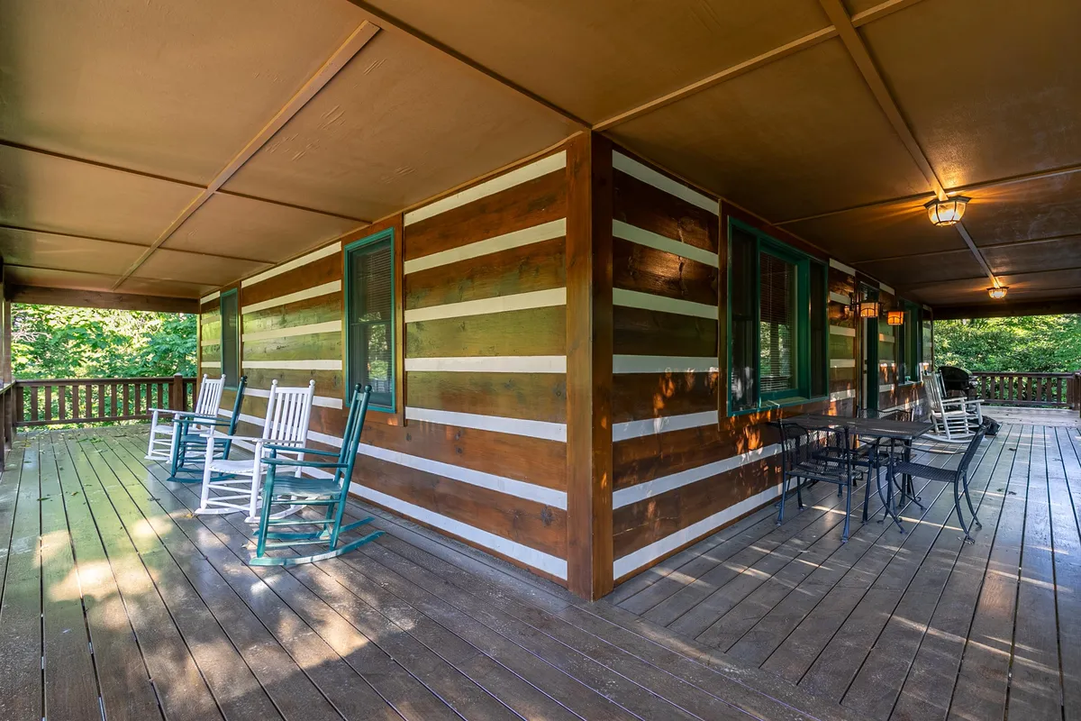 This inviting porch scene showcases classic wooden rocking chairs, a striped wooden wall, and an outdoor dining table, suggesting a peaceful space for sunrise coffees or evening get-togethers. The cozy setting encourages relaxation and taking in mountain views.