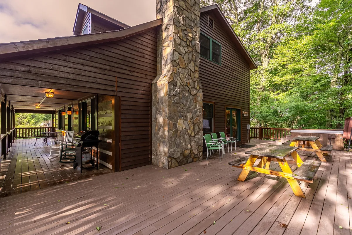 Here, we see a spacious wooden deck with a stone chimney, picnic table, and outdoor seating area, all surrounded by lush greenery. This inviting space is ideal for outdoor dining, barbecues, and socializing after exploring the area's attractions.