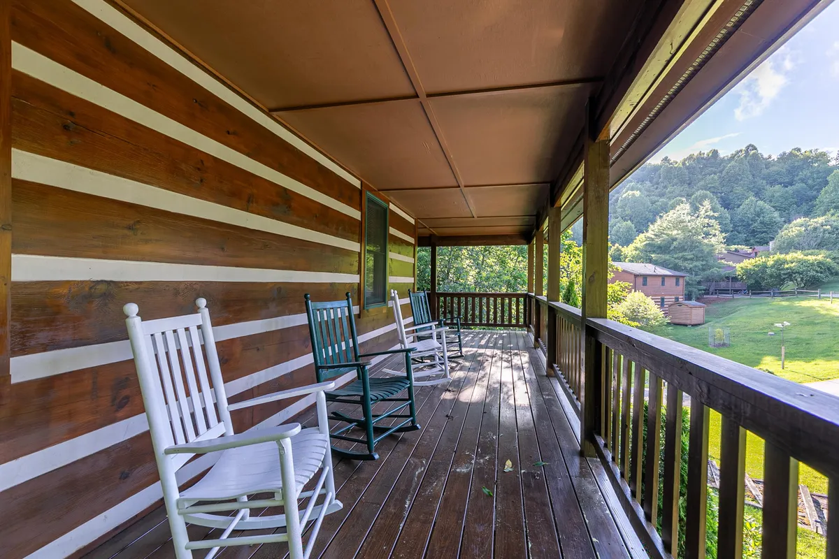 This exterior view focuses on a cozy porch with classic rocking chairs, rustic wooden railings, and lush greenery in the background. The scene suggests a peaceful retreat for enjoying serene mountain mornings or winding down after outdoor activities.
