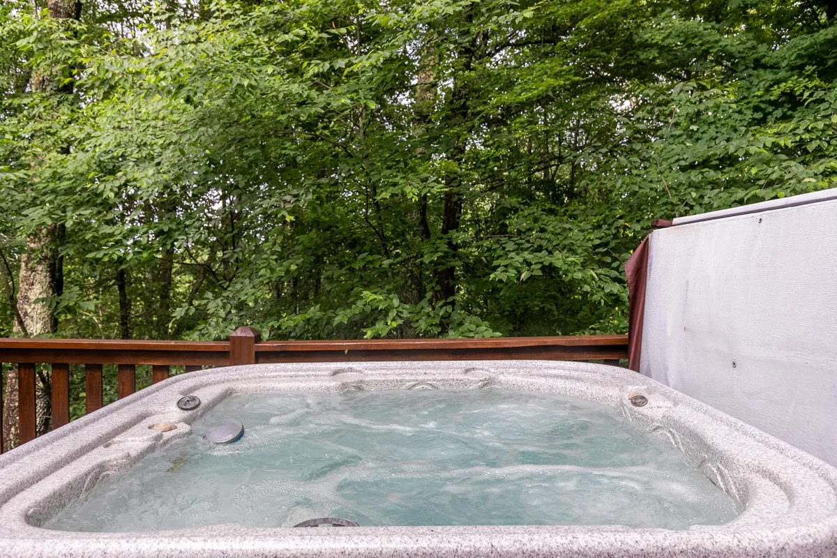 This image showcases a tranquil outdoor deck with a hot tub overlooking the surrounding trees. The serene setting encourages relaxation, whether stargazing at night or enjoying peaceful moments with family after a day of adventure.
