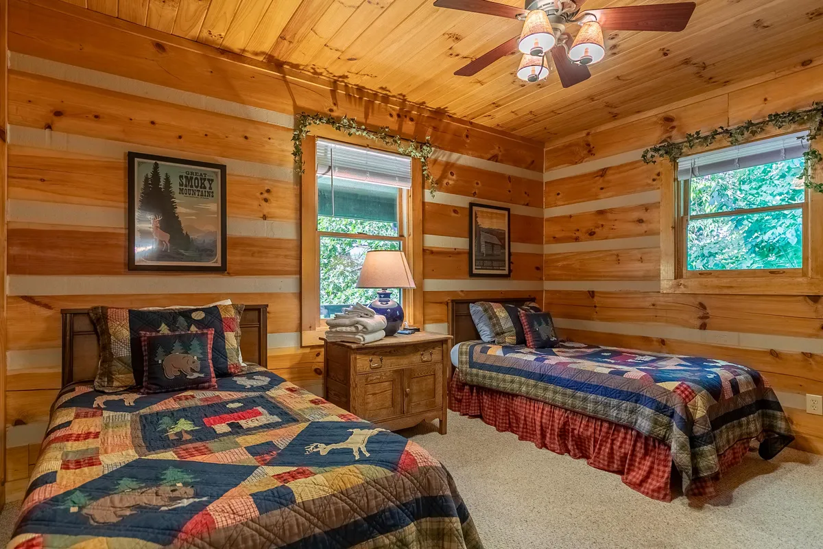 A rustic, intimate corner featuring wooden walls, plaid quilts, a soft lamp glow, and a window looking out to nature. This nook suggests a perfect spot for reading, quiet reflection, or unwinding with a good book.