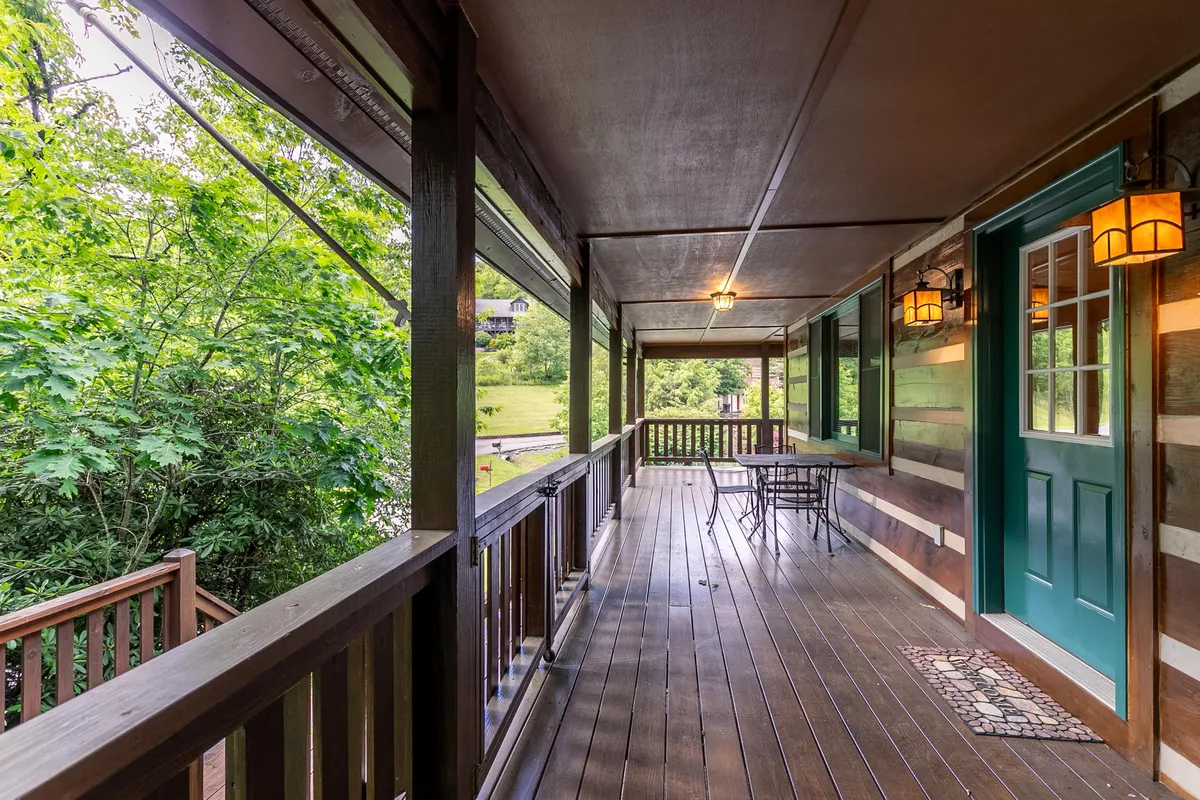 An inviting exterior shot featuring a wooden porch with a green door, outdoor seating area, and surrounding greenery. The porch looks out onto a tranquil, natural setting, ideal for enjoying the fresh mountain air or watching the sunset.