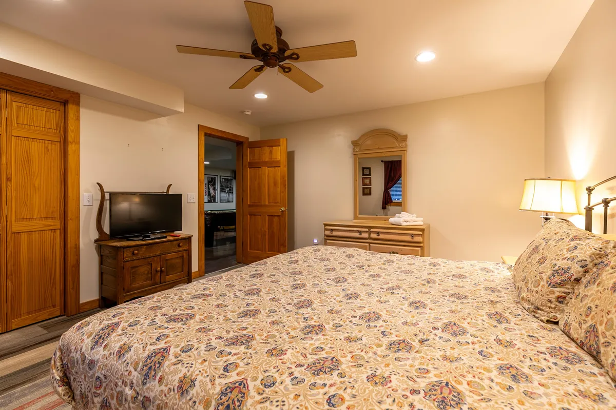 A master bedroom featuring a king-sized bed adorned with patterned bedding, complemented by warm wooden furniture, a wall mirror, and gentle lighting. The atmosphere is serene and cozy, inviting relaxation and privacy.