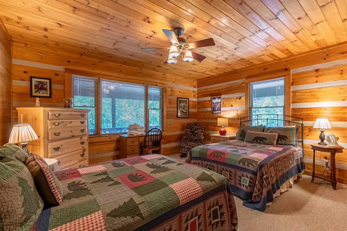 A warmly lit bedroom featuring wooden paneling, cozy bedding with inviting patterns, and windows letting in ample natural light. A nightstand with a lamp enhances the snug, homey atmosphere, suggesting a place to unwind after outdoor adventures.